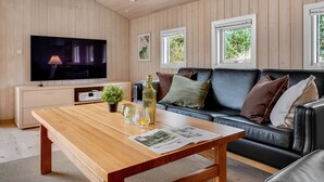 A modern living room with a wooden ceiling, a flat-screen TV, a leather sofa, a wooden coffee table, and a window with a view of greenery. - "Birgita" - 700m from the sea by Interhome (Vejers Strand)