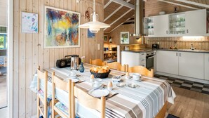 A dining area with a wooden table set for breakfast, a kitchen with white cabinets, and a large abstract painting on the wall.
