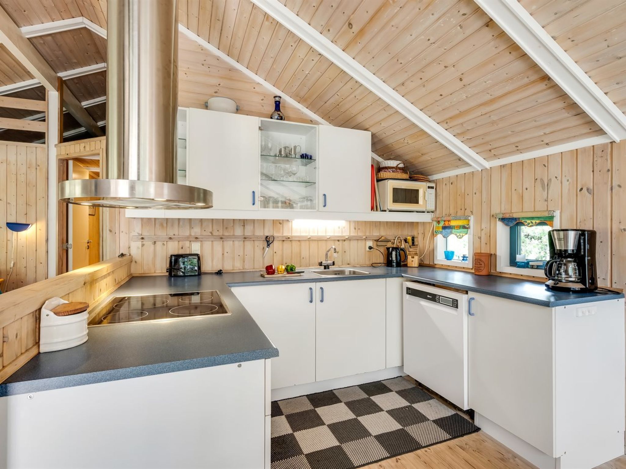 A compact kitchen with white cabinets, a stainless steel range hood, a microwave, and a coffee maker.