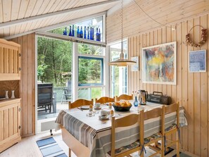 A cozy dining area with a wooden table set for four, a large window with blue glass bottles, and a painting on the wall.
