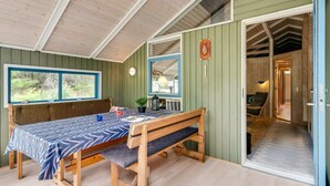A cozy room with a wooden bench, a table with a patterned tablecloth, and a large window overlooking greenery.