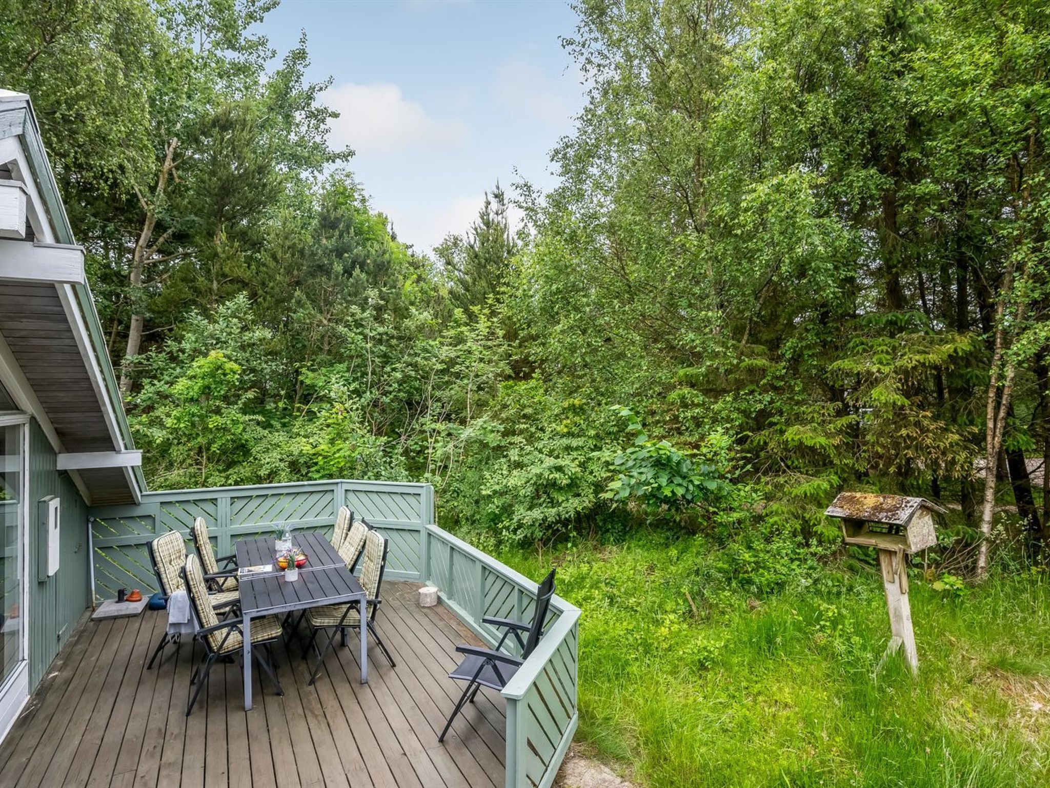 Eine Holzterrasse mit Tisch und Stühlen, umgeben von üppigem Grün und Bäumen.