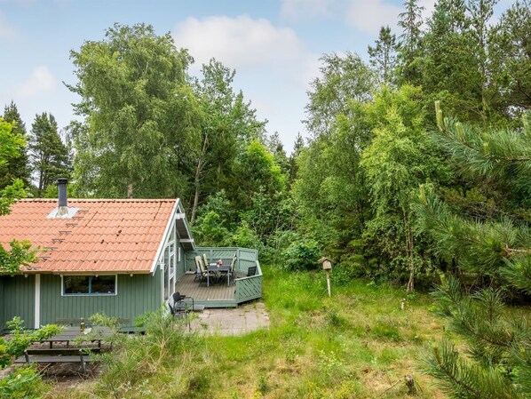 A cabin with a red-tiled roof, a deck with outdoor seating, surrounded by dense forest.