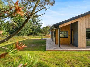 A modern wooden building with a deck, surrounded by a grassy area and trees.
