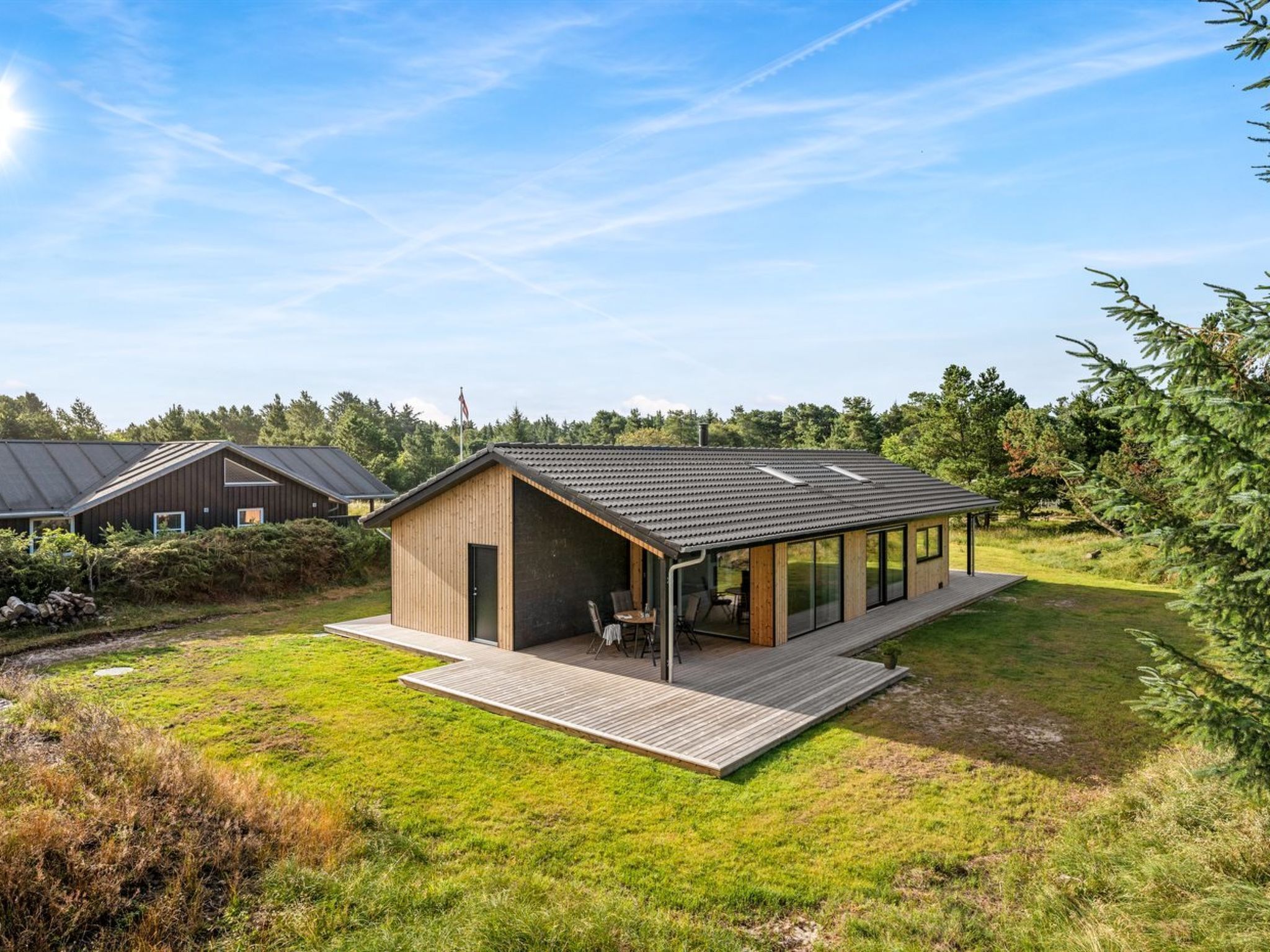 Ein modernes Haus mit einer Terrasse, einer kleinen Sitzecke und einer großen Glasfassade.