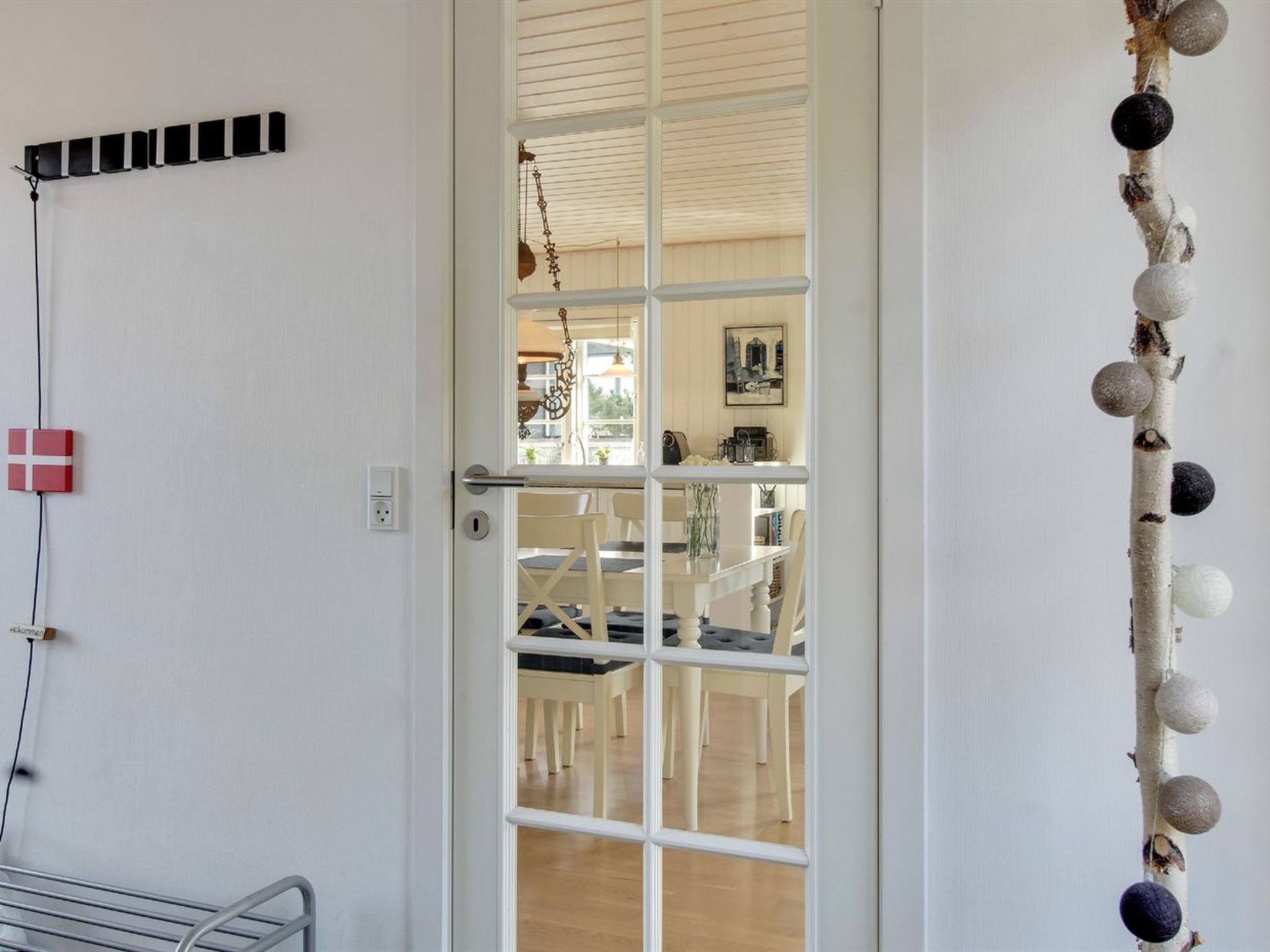 A room with a white door, a small table with chairs, and a wall-mounted shelf with decorative items.