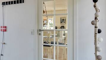 A room with a white door, a small table with chairs, and a wall-mounted shelf with decorative items.