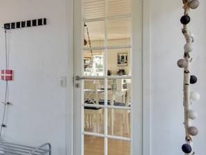 Una habitación con una puerta blanca, una pequeña mesa con sillas y un estante con adornos.