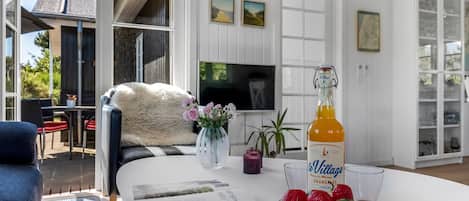 Un salon moderne avec un canapé blanc, une table basse sur laquelle se trouve une bouteille de jus d’orange, un bol de fraises et un magazine.