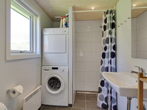 A compact bathroom with a washing machine, a toilet, a sink, and a shower with a polka dot curtain.