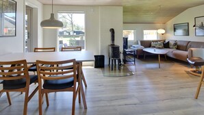 Ein modernes Wohnzimmer mit Essbereich, Kaminofen und großem Fenster für natürliches Licht.