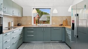 Une cuisine moderne avec des meubles gris, un réfrigérateur en acier inoxydable et une fenêtre donnant sur une maison.