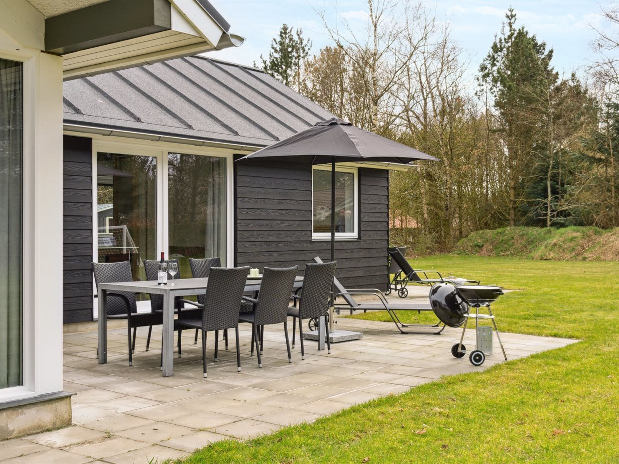 Une terrasse avec une table et des chaises, un barbecue et un espace abrité.