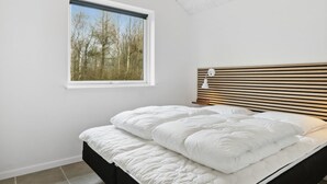 Une chambre à coucher avec un lit, une fenêtre donnant sur des arbres et un luminaire au plafond.