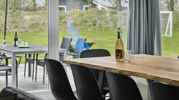 Un coin repas avec une table en bois, des chaises noires, une bouteille de vin et un verre.