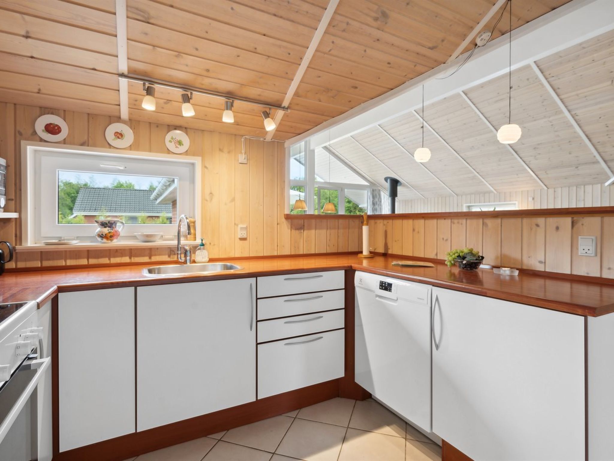 A modern kitchen with wooden cabinets, a large window, and pendant lights.
