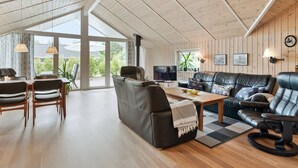 A spacious living area with a high ceiling, wooden walls, a large window, and a cozy seating arrangement.