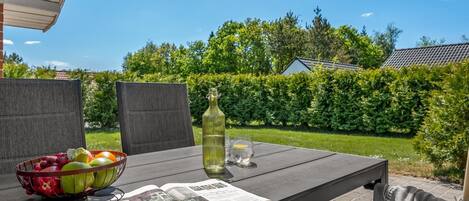Eine Terrasse im Freien mit einem Tisch für zwei Personen, mit Obstschale, Flasche und Zeitung.