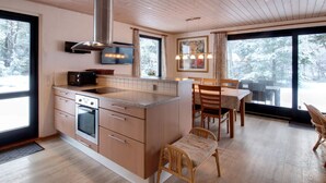 Een moderne keuken met houten kastjes, een ingebouwde oven en een magnetron. Er is een eethoek met een tafel en stoelen.