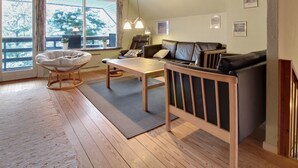 Een gezellige woonkamer met een houten plafond, een leren bank, een ronde fauteuil, een tafel en uitzicht op de natuur door grote ramen.