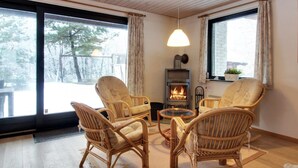 Een gezellige woonkamer met rieten stoelen, een glazen salontafel en een houtkachel.