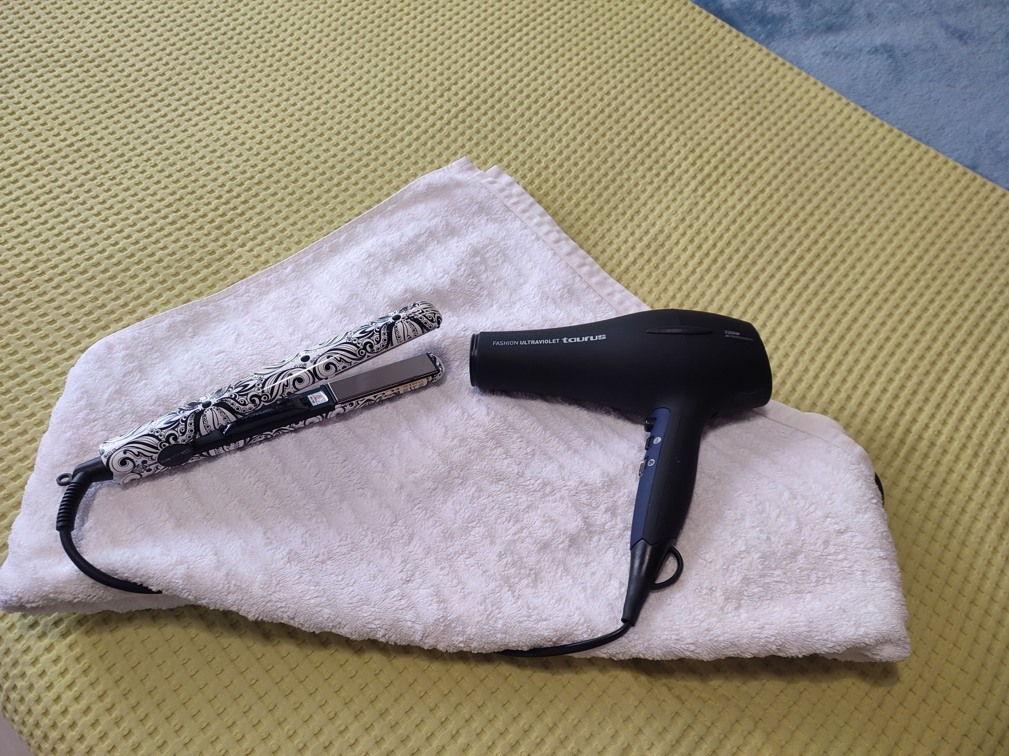 A hair dryer and a patterned umbrella on a white towel on a textured surface.