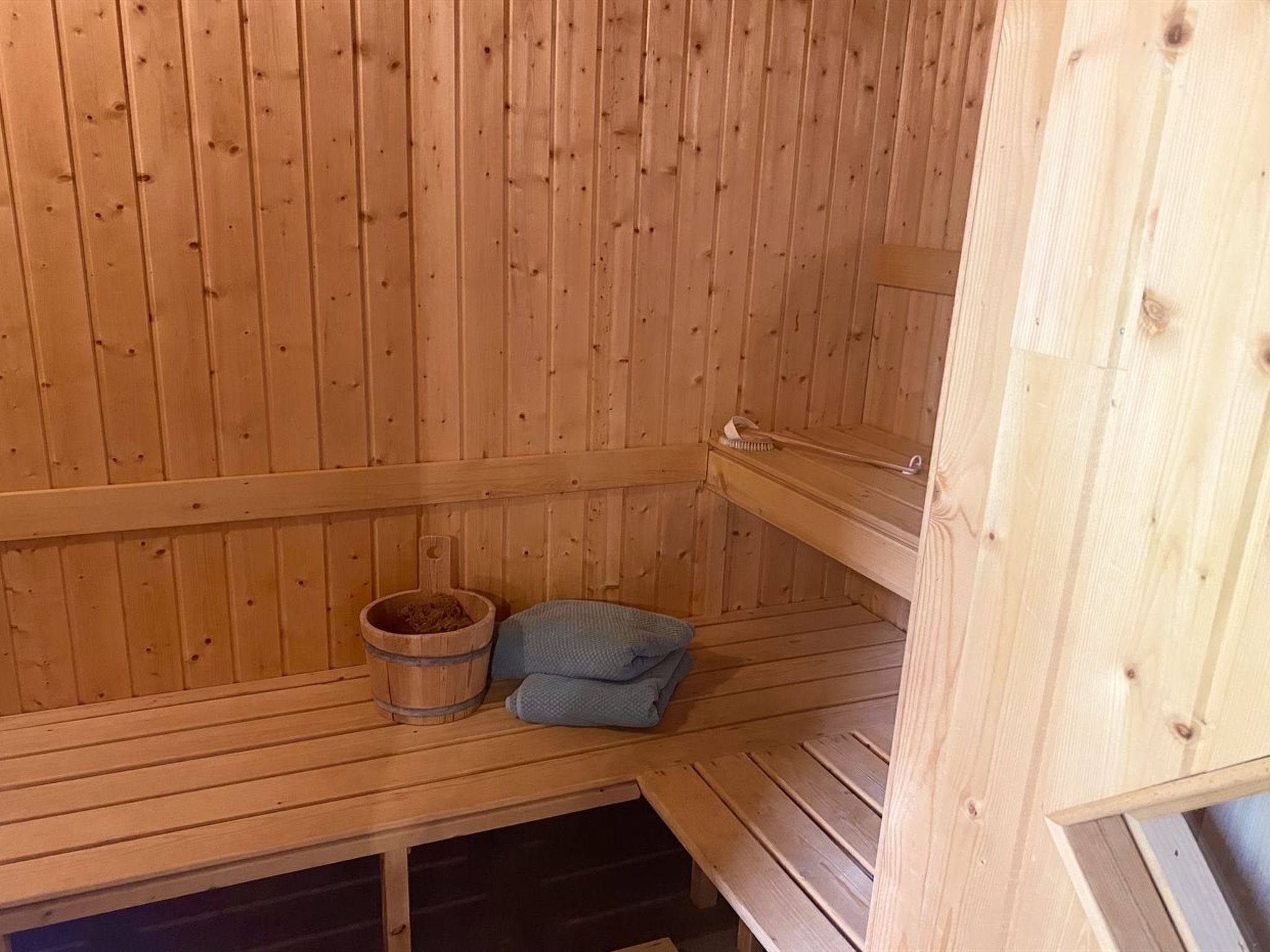 Una sauna de madera con bancos, un balde de madera y una toalla.