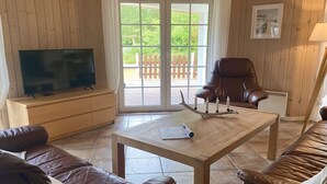 A cozy living room with a television, leather sofas, a wooden table, and a large window with a view of greenery. - "Orpah" - 2.5km from the sea by Interhome (Rømø)