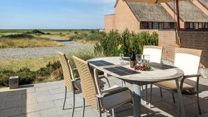 Eine Terrasse im Freien mit einem runden Tisch, Korbstühlen und einem großen Sonnenschirm.