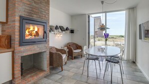 Ein gemütliches Zimmer mit Kamin aus Ziegelsteinen, Korbmöbeln, einem Esstisch und Blick auf die Landschaft.