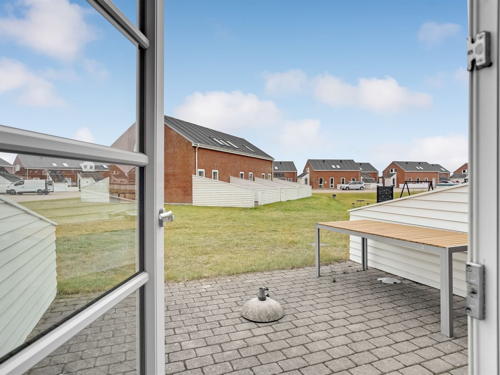 A modern building with a brick facade, a flat roof, and a paved courtyard with a small round object.