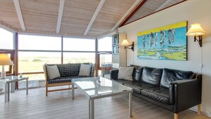 A spacious living room with a glass coffee table, a black leather sofa, and a view of the outdoors through large windows. - "Alim" - 300m from the sea by Interhome (Rømø)