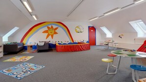 Een kinderspeelkamer met een kleurrijke muurschildering, een box, een tafel vol speelgoed en een bank.
