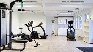 Een fitnessruimte met trainingsapparatuur, een hometrainer en een kleine kitchenette.