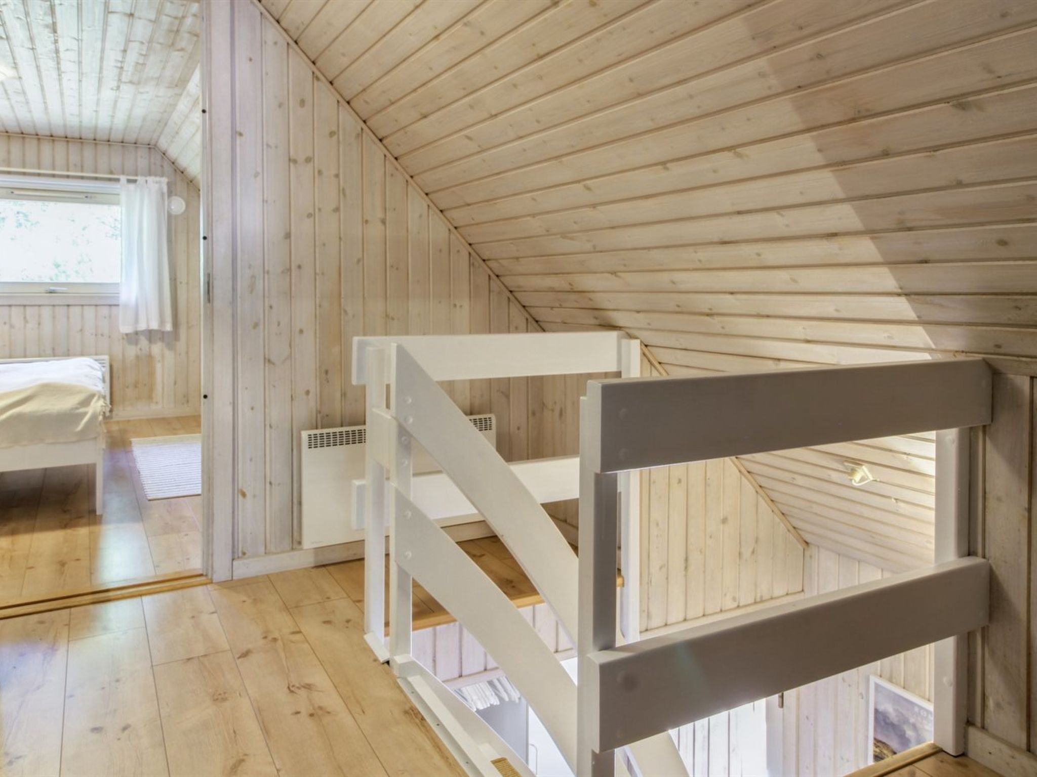 Une pièce avec un plafond en pente, des murs en bois, un lit et un escalier en métal blanc.