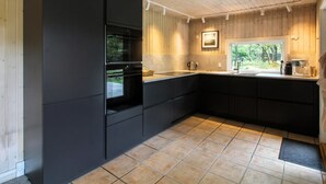 Une cuisine moderne avec des meubles de couleur sombre, un four encastré et une fenêtre donnant sur l’extérieur.
