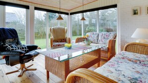 Una habitación acogedora con una mesita de vidrio, muebles de mimbre y una silla con cojín estampado.
