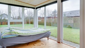 Un dormitorio con cama, suelo de madera y ventanas amplias con vistas al jardín.