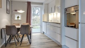 A modern kitchen with white cabinets, a built-in oven, and a dining area with a table and chairs. - "Anouk" - 1.7km from the sea by Interhome (Rømø)
