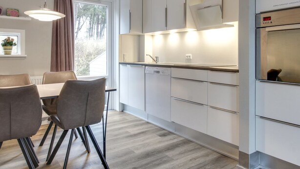 A modern kitchen with white cabinets, a built-in oven, and a dining area with a table and chairs. - "Anouk" - 1.7km from the sea by Interhome (Rømø)