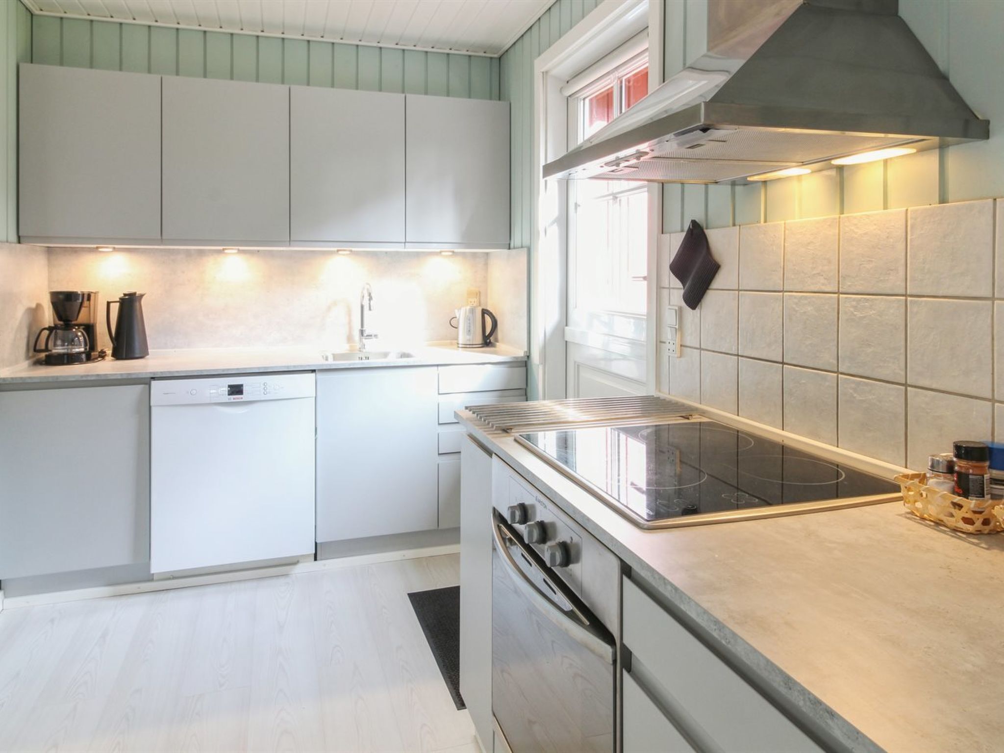 A modern kitchen with white cabinets, a stainless steel range hood, and a built-in oven.