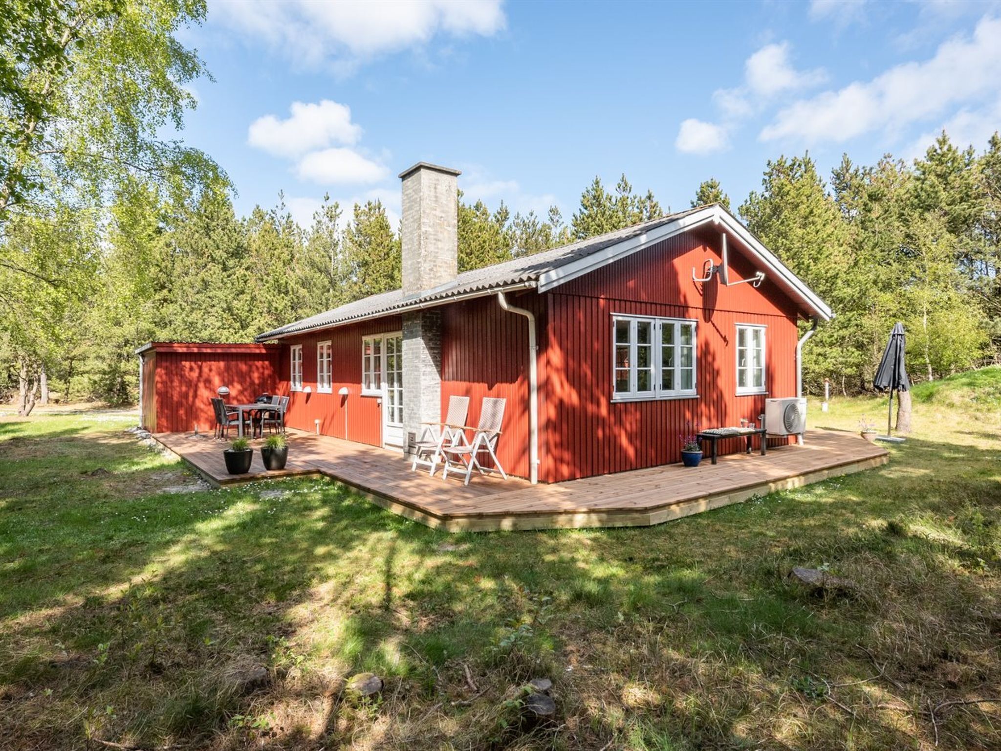 En rød træhytte med terrasse, skorsten og en patio med stole og bord.