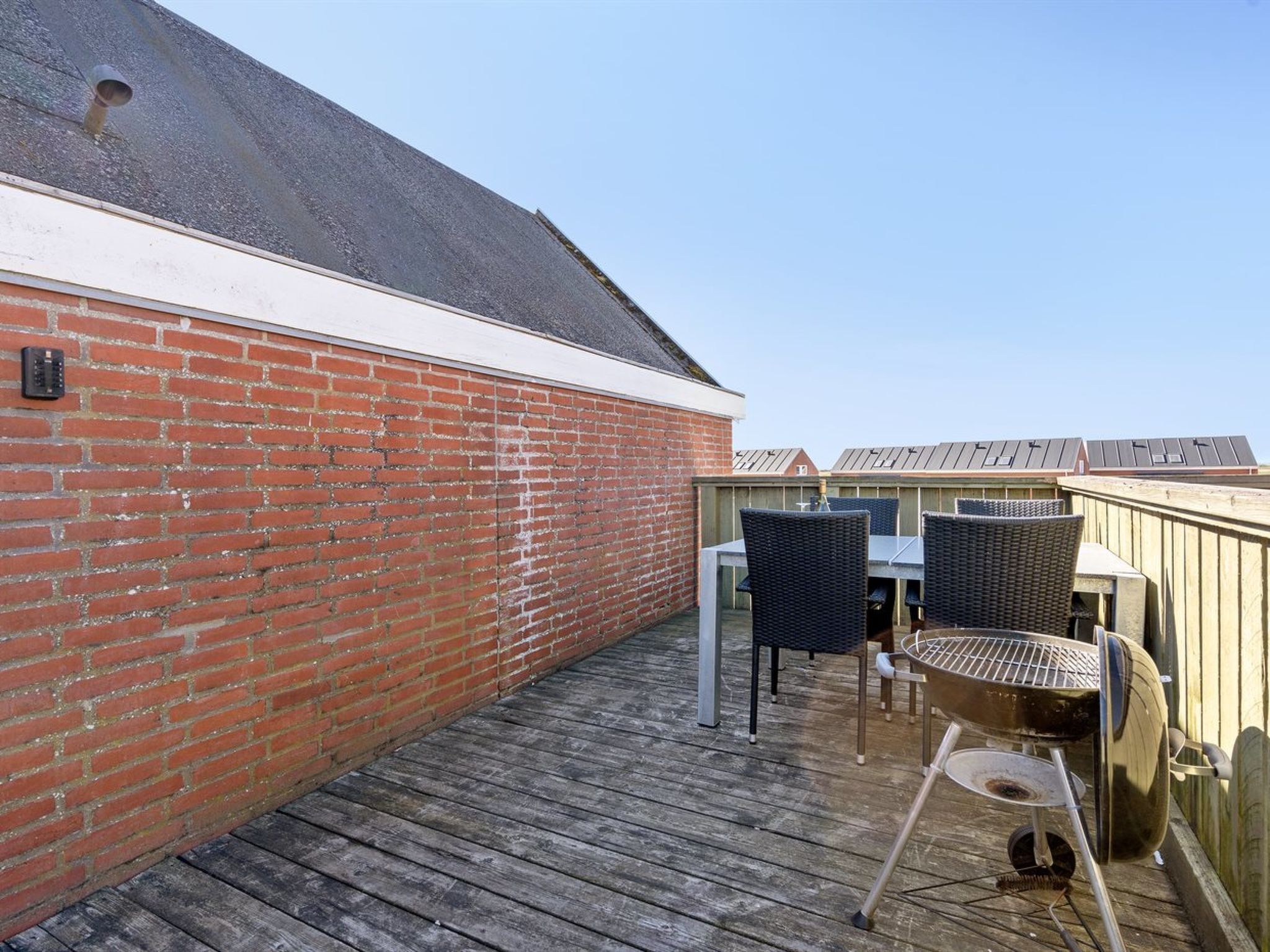 Une terrasse en bois avec un mur en briques, deux fauteuils en osier et un barbecue.