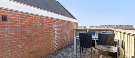 Une terrasse en bois avec un mur en briques, deux fauteuils en osier et un barbecue.