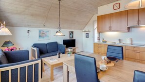 Un saló acollidor amb un sofà, taula de menjador i zona de cuina amb armaris de fusta i un rentapeus.