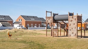 Un parc infantil amb una estructura per escalar i un tobogan, envoltat de cases amb teulades inclinades.