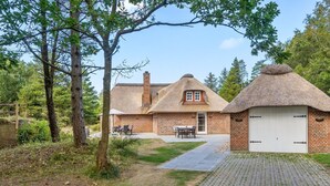 A rustic house with a thatched-roof extension, a brick chimney, and a paved driveway leading to a garage.