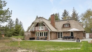 A two-story house with a thatched roof, a brick exterior, and a covered patio area with outdoor furniture.