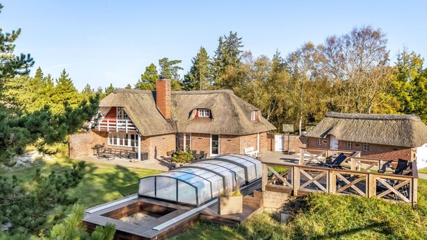 A thatched-roof house with a greenhouse, wooden deck, and outdoor seating area.