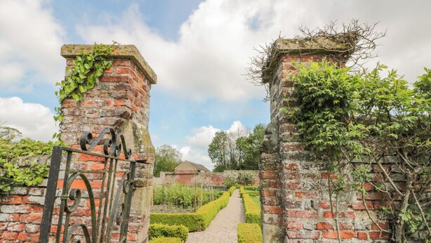A pathway leading through a garden with brick walls and metal gates. - Wolds Way (Driffield)